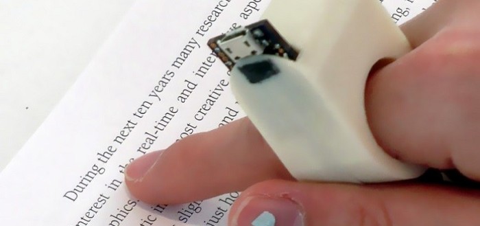 imagem do anel inteligente no dedo indicador de uma pessoa sobre uma folha com texto impresso
