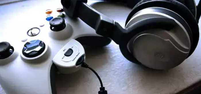 imagem de um controle do video game xbox com um fone de ouvido grande com abafadores de som acoplado a ele sobre uma mesa