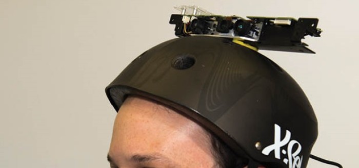imagem de um rapaz deficiente vvisual vicual com um capacete normalmente utilizado por skatistas com o sensor de movimento kinet usando no xbox preso no topo com um fio indo para as costas, onde há uma mochila